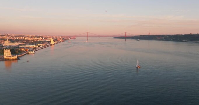Tagus River and Lisbon shoreline with sailboat at sunset, aerial drone wide shot, Portugal