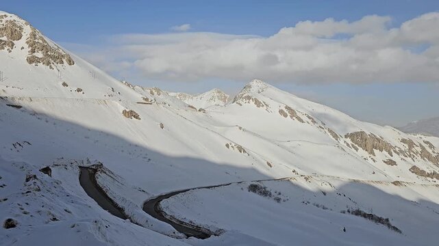 Winding mountain road snakes through deep snow-covered slopes and rugged peaks under vivid blue sky with scattered clouds in breathtaking winter highland scenery.
📍Hawraman Takht, Kurdistan 