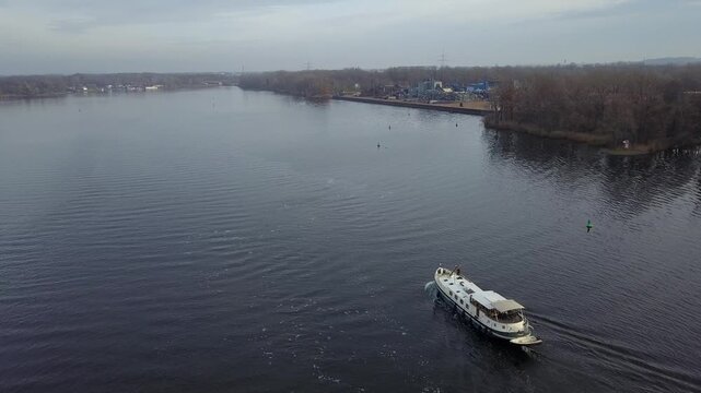 Zoom in aerial of boat advancing on Elbe Labe river surrounded by farmland and autumn trees under clear sky.