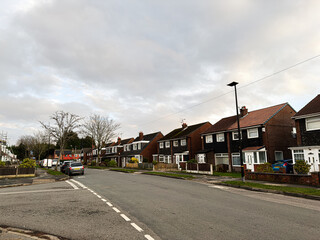 Obraz premium Residential street in Manchester UK with row houses, parked cars, and a cloudy sky