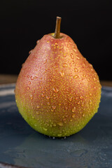 wet ripe green-red ripe pears on a blue ceramic bowl on the table, several ripe hard and juicy pears are lying on a bowl on the table, the pears are covered with drops of water