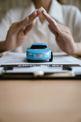 Hands protect two toy cars placed on a car insurance document, symbolizing vehicle protection, accident coverage, and auto insurance policy planning. © Natthawadee