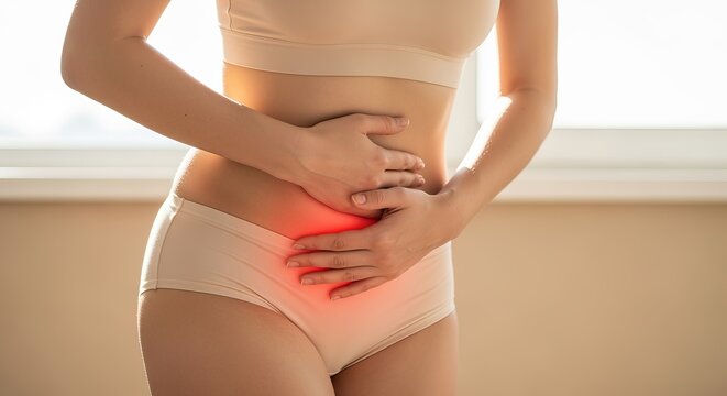 Young woman in beige innerwear expressing discomfort due to menstrual cramps in her lower abdomen.