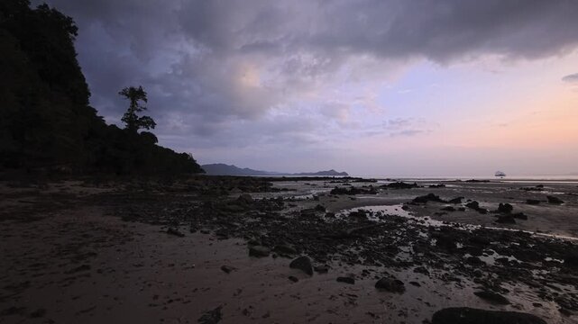 Sunset over rocky tidal flat with dark clouds and distant islands in Thailand