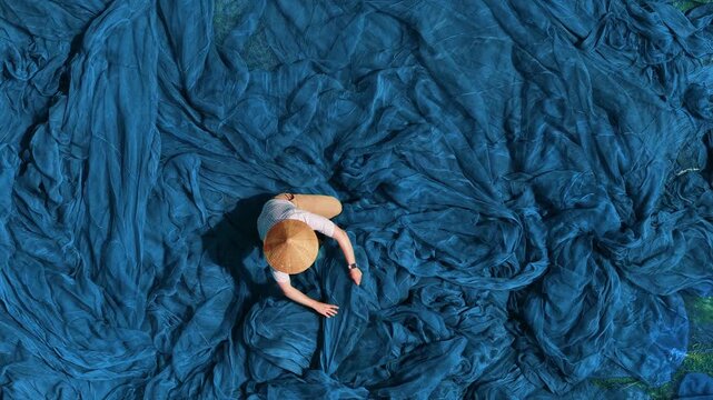 Male fisherman sorting green fishing nets in Vietnam aerial view.