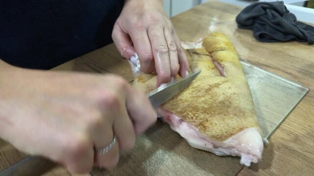 A woman scrapes pieces of pork skin with fat remnants with a knife for freezing. Home pork preparation. Close-up.