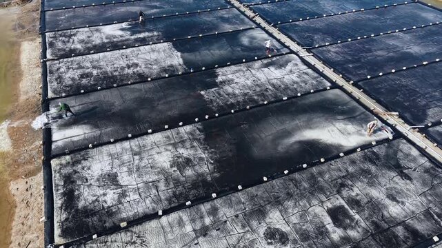 Aerial top view of people working on traditional salt mining fields industry in Vietnam.