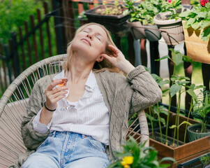 Relaxed blonde mid adult woman with glass of rose wine on a summer blooming terrace