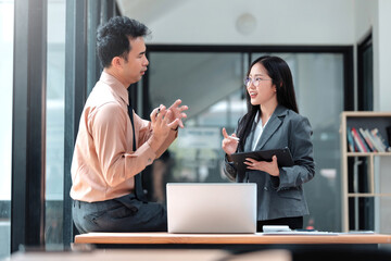 Fototapeta premium Asian business people collaborating, a man explaining with hand gestures while a woman listens with a tablet