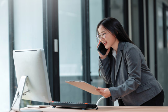 Asian businesswoman engaging in a phone conversation while reviewing documents, reflecting communication and multi tasking in her professional career