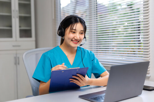 Smiling healthcare professional in scrubs telecommuting, providing online medical advice and support via laptop and headset