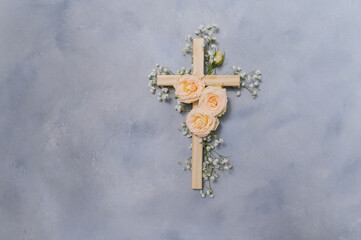 Wooden christian cross with pink roses and gypsophila flowers on a dark shadow wall representing...