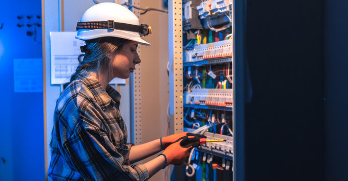 Woman electrician repairs electrical panel in technical room. Panel maintenance.