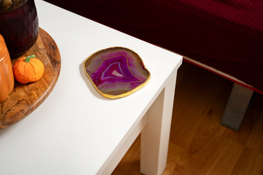Pink agate coaster placed on the side of a white coffee table in a simple, everyday home interior, combining natural stone and clean modern decor. Energy, grounding, spirituality, minimalism