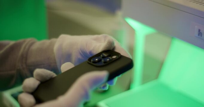 Hands in white gloves applying a screen protector to a smartphone under UV light