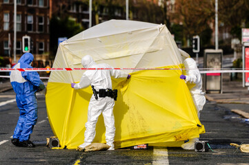 Three forensics officers position an examination tent over a crime scene to preserve evidence prior to a detailed examination.  © Stephen