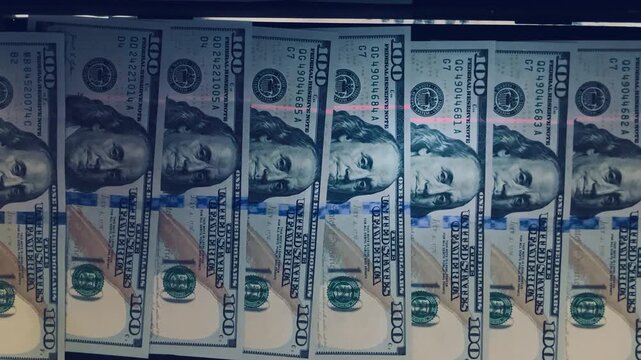 Row of one hundred dollar bills being checked for authenticity with UV light