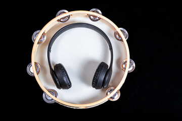 Black headphones placed inside a tambourine on white background with dark area. Audio equipment for music listening