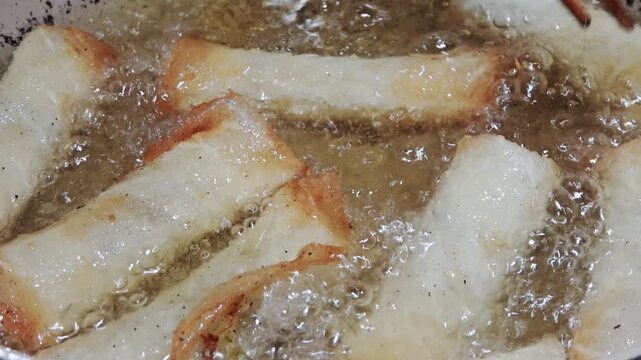 Spring rolls being deep-fried to a golden crisp.