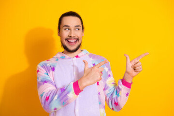 Playful man in pastel unicorn pajama jumpsuit smiles while pointing at the bright yellow background