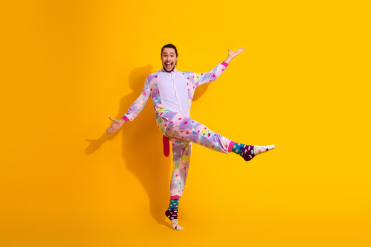 Playful man in colorful star pajama jumpsuit poses happily against bright yellow background and shows energetic motion