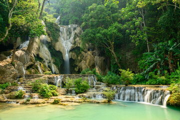 Bright sunlight highlights the tiered limestone cascades and turquoise pools of Kuang Si Waterfalls in northern Laos. Dense tropical forest surrounds the flowing water, creating a vivid and serene © Florent