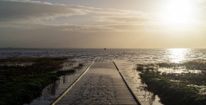 Wooden pier covered with water and sand against the backdrop of the sea with sunlight from the side