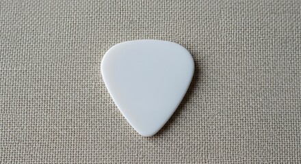 Fototapeta premium A plain white triangular guitar pick resting on a textured fabric background