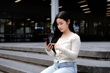 Obraz premium Asian student relaxing on campus stairs using smartphone