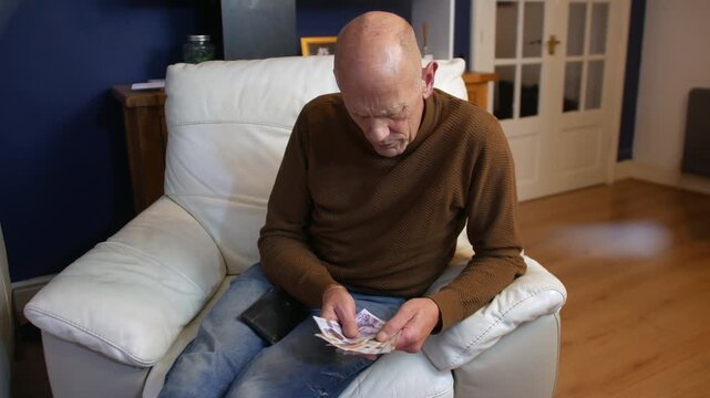 A mature man counting money at home The bald senior male is counting english pound notes in cash at home