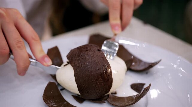 Close up of a coconut shaped dessert with a chocolate shell being cut open to reveal a creamy interior