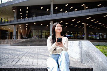 Fototapeta premium Asian student relaxing on campus stairs using smartphone