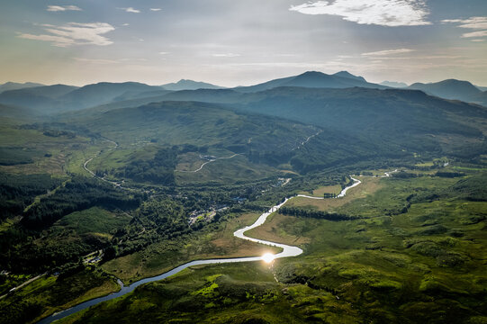 Aerial view of a winding river through the Scottish Highlands landscape at sunset