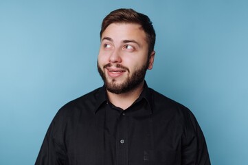 Obraz premium Man with beard smiles thoughtfully against a vibrant blue background while wearing a black shirt during a creative studio session