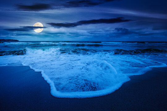 tide rolling on the sandy beach at night. full moon over sea waves beneath a cloudy sky. empty calm scenery in summer. loneliness concept. mysterious image for wallpaper or book cover use