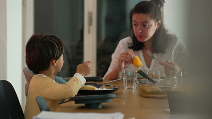 Fototapeta premium Mother and young boy sharing a conversation during family mealtime at a dining table, engaged interaction, nurturing bond, and relaxed indoor atmosphere