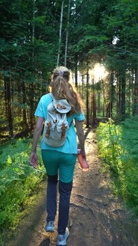 Woman with backpack walking on sunlit forest path in Norway. Authentic lifestyle, mental health wellness and sustainable solo travel concept in Northern Europe.