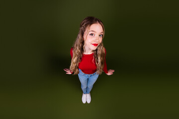 Young woman in red top and jeans floats against green background smiling up
