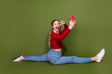 Young woman in red crop top performs a split selfie against green backdrop with a bold smile and...