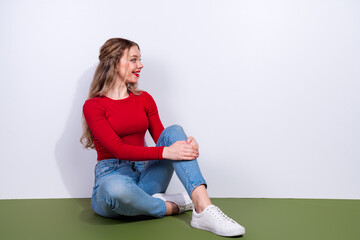 Young woman in red top sits on green floor smiling with crossed legs in casual fashion lifestyle...