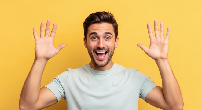 Excited young man with open mouth and hands raised, showing ten fingers against yellow background