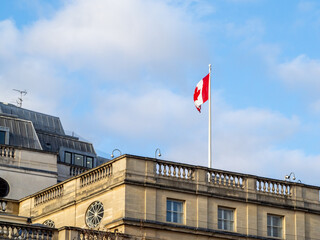 The Canadian national flag flying against the blue sky on top of the Canadian embassy