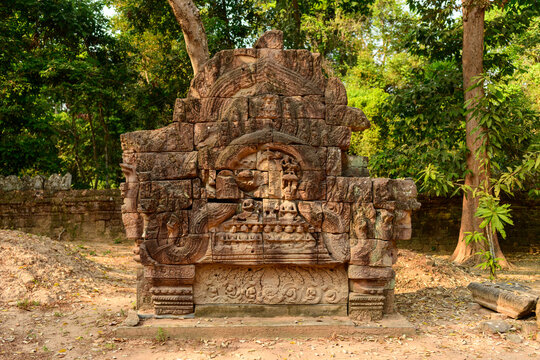 Intricately carved sandstone lintel stands amid the forest at Ta Som temple in Cambodia's Angkor region. Warm sunlight highlights the detailed bas-relief and weathered stone against a backdrop of