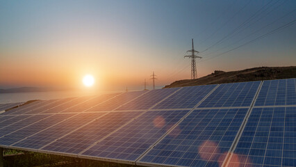 Solar panels generating clean energy at sunset with power transmission lines in the background. © banphote