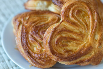 Fototapeta premium Golden brown sweet bun on a plate. Freshly baked yeast dough pastry. Heart-shaped puff pastry with sugar