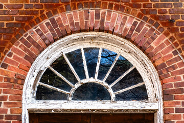 Peeling paint adorns arched transom window surrounded by bricks