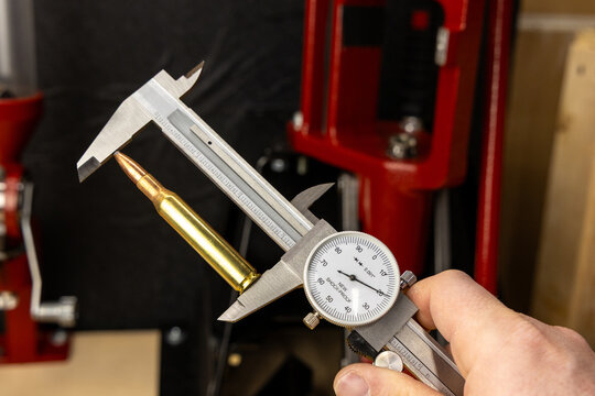 Precision measurement of a rifle cartridge with a dial caliper, emphasizing accuracy and detail