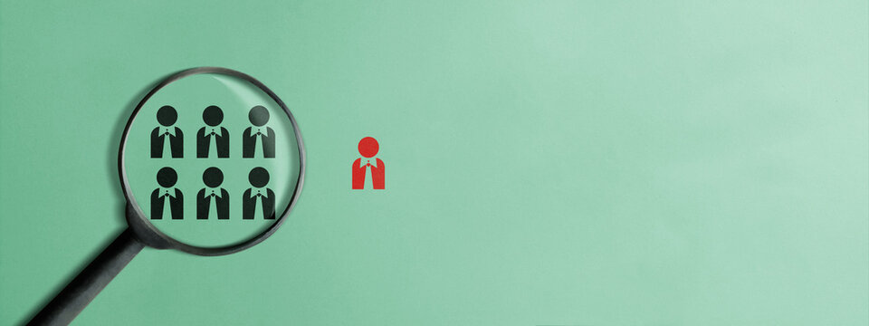 A magnifying glass focusing on black employee icons with one distinct red figure, representing recruitment, talent scouting, human resources, and the search for the perfect candidate
