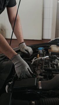 Medium vertical shot of unrecognizable male mechanic checking up car engine, pointing to spark plugs and ignition, instructing apprentice and explaining mechanisms while working in garage