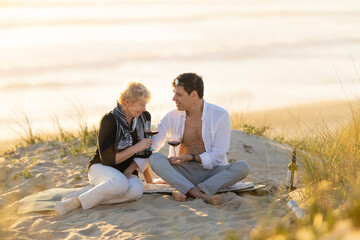 Fototapeta premium Senior woman and man enjoying beach picnic with wine